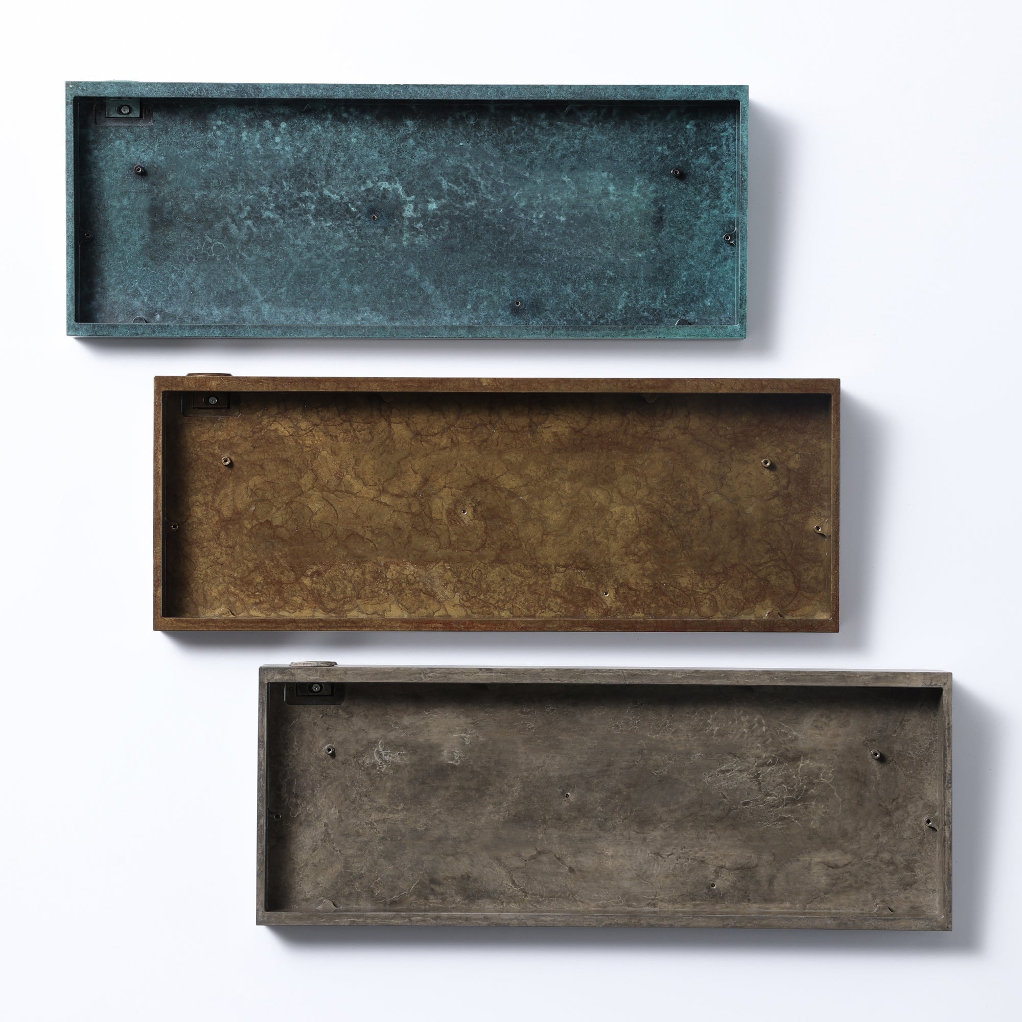 Three keyboard cases showing blue-green, bronze and raw metal finishes